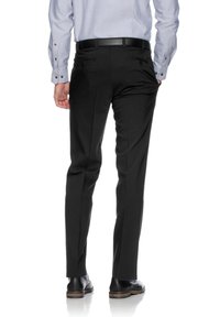 Schwarze Anzughose mit tailliertem Schnitt, ausgestattet mit zwei Gesäßtaschen, Bügelfalten und einer glatten Textur, kombiniert mit glänzenden schwarzen Anzugschuhen.