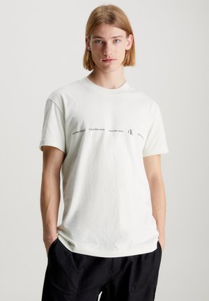 Camiseta blanca de algodón con manga corta y escote redondo. En la parte delantera presenta un texto repetido en negro que dice "Calvin Klein Jeans" y el logotipo.