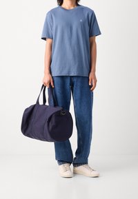 Modré tričko s krátkým rukávem a logem kola, spárované s volnými denimovými džíny a kulatou námořnickou taškou s dvěma uchy. Béžové tenisky.