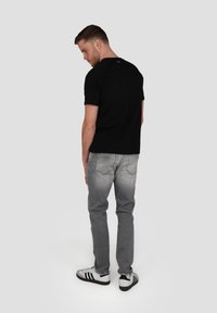 T-shirt noir à manches courtes, associé à un jean gris clair. Le modèle porte des baskets rayées noir et blanc. Tenue simple et décontractée.