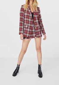 Rood en wit geruite blazer met franjerand, sluiting met één knoop en twee opgestikte zakken, gecombineerd met zwarte enkellaarsjes.