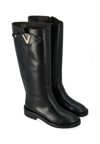 Bottes noires en cuir montant jusqu'au genou avec une finition lisse, bout carré et accent en métal doré en forme de V sur le côté. Semelle plate pour plus de stabilité.
