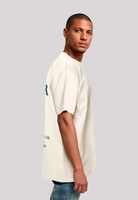 Crème-kleurige oversized t-shirt van katoen, met groene tekst en graphics op de voorkant en achterkant, met korte mouwen en een ontspannen pasvorm.