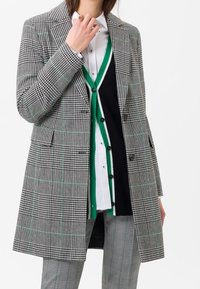 Blazer a scacchi grigi e neri con dettagli verde, vestibilità su misura, design doppiopetto, con due tasche frontali e colletto a punta.