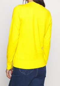 Heller gelber Pullover mit langen Ärmeln, gerippten Bündchen und Saum, aus einem weichen, strukturierten Stoff. Mit klassischem Rundhalsausschnitt.