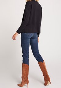 Zwart gebreide trui met een split aan de achterkant, gecombineerd met donkerblauwe jeans en bruine suède laarsjes tot de knie met een puntige neus.