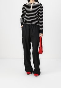 Randig svart och beige långärmad polo tröja, lösa svarta cargobyxor, röd handväska och röda spetsiga skor med metalliska spetsar.