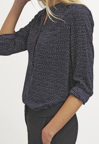 Camicia blu navy con bottoni e pois bianchi, dotata di colletto alla cinese e maniche arrotolate. Tessuto morbido e leggero con una vestibilità rilassata.