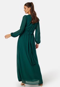 Grünes Chiffon-Maxi-Kleid mit langen Ärmeln, gerafftem Taillenbund und einer gebundenen Akzentuierung am Rücken. Sanfter Stoff und fließende Silhouette.