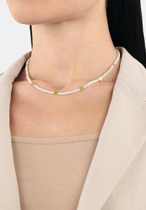 Parelsnoer met witte kralen en gouden hartvormige accenten, ontworpen met een subtiele, gladde textuur, gedragen boven een beige top.