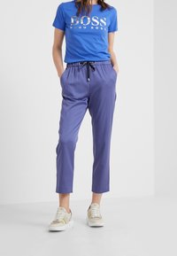 Niebieska bawełniana koszulka z metalicznym logo "BOSS", w połączeniu z purpurowymi, lekkimi spodniami z elastycznym pasem oraz beżowymi sneakersami z akcentami.