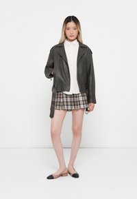 Mørk grå skinnbikerjakke med glidelåsdetaljer, hvit knappskjorte, rutete plisserte miniskjørt og to-farget slingback-flats.