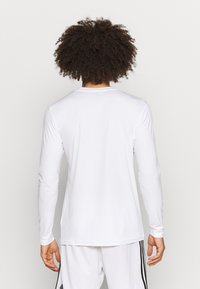 Langzaam, wit sportshirt met lange mouwen, een gladde textuur, ronde halslijn en een slim fit. Voorzien van ingezette mouwen voor meer bewegingsvrijheid.