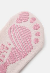 Calzino rosa chiaro con un motivo di grip in gomma testurizzata a forma di impronta. La superficie presenta accenti rialzati orizzontali e circolari.