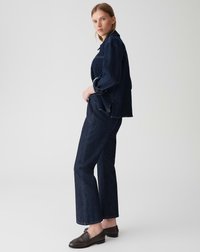Veste en denim foncé et pantalon à coupe décontractée, avec des coutures visibles et des poches latérales. Des mocassins marron complètent le look.