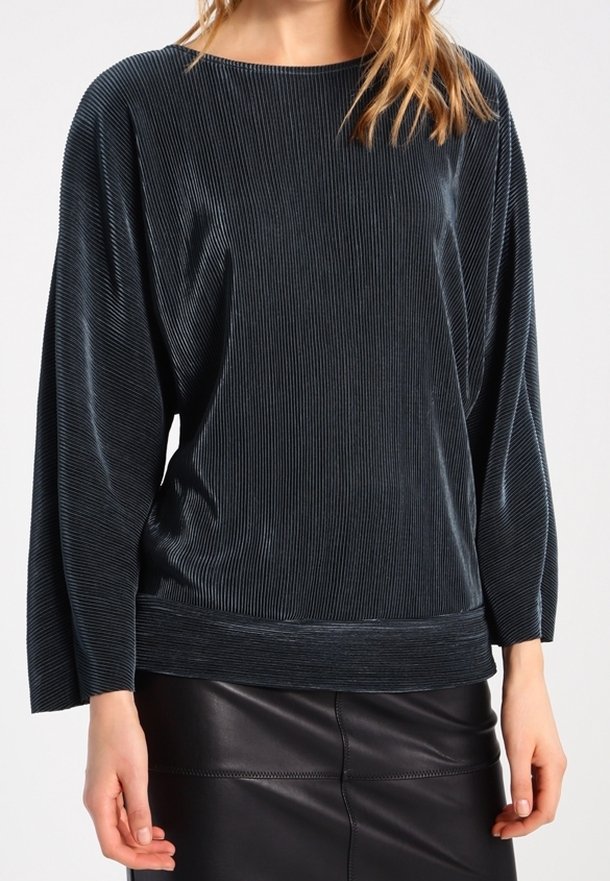 Pullover in velluto blu scuro con texture a coste, maniche ampie e scollatura a barca. Abbinato a una gonna in pelle nera.