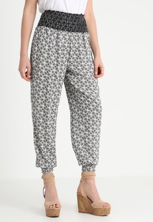 Mujer que lleva pantalones sueltos con estampado en blanco y negro, cintura fruncida y sandalias cuña beige con pulseras en el tobillo.