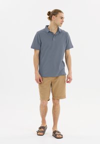 Manskortärmad polo i grå bomull med krage, kombinerad med beiga knälånga shorts och bruna sandaler.