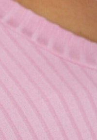Primo piano di un tessuto a coste rosa chiaro, caratterizzato da un motivo testurizzato con linee verticali. Il colletto ha una forma morbida e arrotondata.