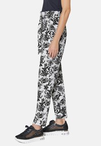Schwarz-weiße Blumenmuster-Hosen mit einem Bindegürtel, aus leichtem Stoff gefertigt, kombiniert mit schwarzen sportlichen Sneakers mit transparenten Akzenten.