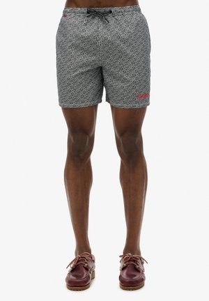 Costumi da bagno in bianco e nero con un motivo di testo ripetuto, vita elastica e cordino. Finiti con un accento del logo rosso.