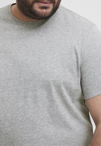 Tricou gri cu mâneci scurte, fabricat dintr-un material moale, având un decolteu rotund și o suprafață netedă, ușor texturată.