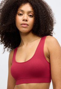 Hladký bordový športový podprsenka so širokými ramienkami a bezšvovým dizajnom. Tkanina je mäkká a elastická, čo poskytuje pohodlné nosenie.