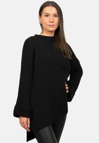 Maglione nero in maglia con texture a costine, caratterizzato da un collo rotondo e maniche svasate. L'orlo è asimmetrico, con una lunghezza maggiore sul retro.