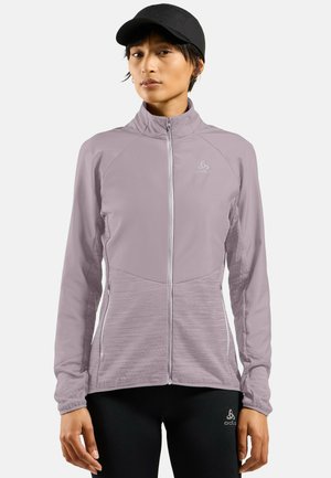 Light purple athletic zip-up jacket with long sleeves, textured fabric, and side pockets. Paired with black leggings and a cap.