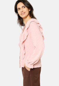Light pink blouse with a textured finish, featuring ruffled accents along the front and sleeves, button closures, and a relaxed fit.