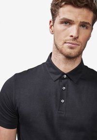 Sort polo-shirt lavet af bomuld, med en krave, tre-knaps front åbning og en glat, struktureret stoffinish.