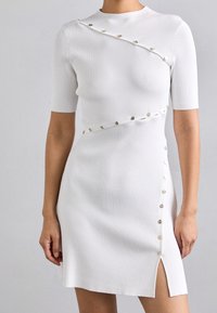 Valkoinen ribbikuvioinen mekko lyhyillä hihoilla, jossa on vinonappiyksitys ja sivurao. Sileä pinta metallinappikoristeilla.