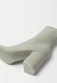 Jasnoszare botki za kostkę o gładkiej, matowej fakturze, z szerokim słupkowym obcasem i bezszwowym wykończeniem. Brak widocznych elementów metalowych lub wzorów.