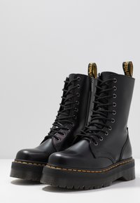 Schwarze Lederkampstiefel mit einer dicken strukturierten Sohle, sichtbarem Schnürverschluss und einem gelben Marken-Ziehlasche oben.