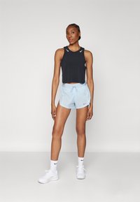 Top corto sin mangas negro y pantalones cortos deportivos azul claro con cordón. Las zapatillas blancas y los calcetines tienen logotipos de Nike.