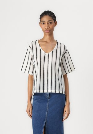Striped short-sleeve top in white and black, featuring a V-neck and textured fabric. Paired with a denim skirt with a front slit.