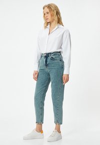 Ljust blå denim högmidjade jeans med smal passform, fransade fållar, kombinerade med en vit skjorta med knappar och vita sneakers.