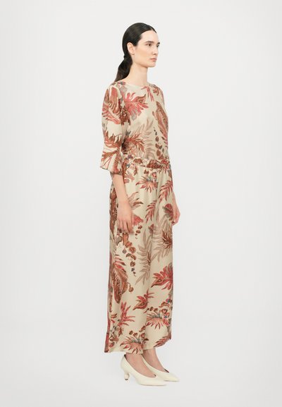 Beige kjole med blomstermønster, tætsiddende talje, ærmer til albuen og et svajende design; parret med hvide sko med runde hæle.