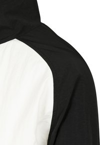 Svart och vit huvan jacka med en strukturerad yta; har en svart panel på axeln som övergår till en vit kropp.