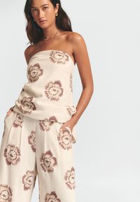Beige strapless topp och vida byxor, båda med bruna blommönster. Tillverkade av textil med struktur, designade med fickor och avslappnad passform.