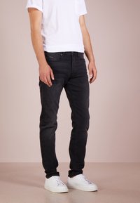 Svarta jeans i denim med smal passform, med klassisk femficksdesign och en slät textur, kombinerat med vita sneakers och en enkel vit t-shirt.