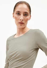Olivgrünes Langarmoberteil mit rundem Halsausschnitt, aus einem glatten Stoff gefertigt; taillierte Form mit dezenten Raffungselementen auf der Vorderseite.