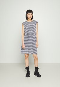 Vestido riscado em azul-marinho e branco, de mangas curtas, com cintura ajustada e cordão. Combinado com botas de combate pretas com atacadores.