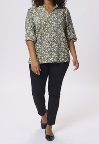 Bluzka o kwiatowym wzorze, lekka, w ciemnozielonym i kremowym kolorze, z dekoltem w serek i rękawami trzyczwartowymi, zestawiona z dopasowanymi czarnymi spodniami.