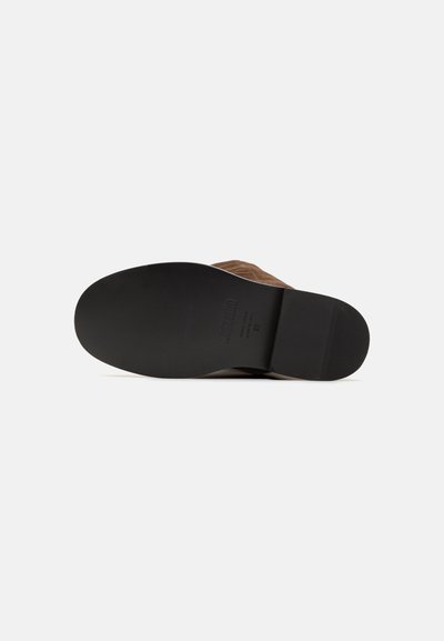 Stivale in suede marrone con suola nera piatta. Presenta una finitura texturizzata e punta arrotondata. Nessun marchio o elemento decorativo visibile.