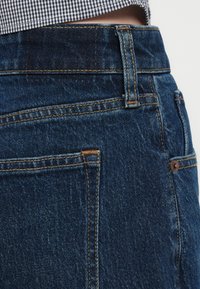 Mørkeblå denimjeans med klassisk snit. Har synlige syninger, diskrete hardware-detaljer og en talje i mellemhøjde.