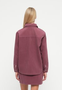 Σ ακάκι από χονδρή καμπαρντίνα σε απαλό μωβ χρώμα, με γιακά, μακριά μανίκια και κουμπωτές μανσέτες; υφασμάτινη υφή με κάθετες ραβδώσεις.