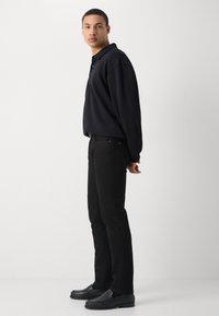 Polo negro de manga larga, jeans negros de corte recto y mocasines negros. Tejido suave, diseño minimalista y silueta ajustada.