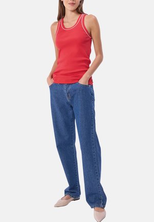 Débardeur rouge avec bordure blanche, associé à un jean bleu ample. La tenue est complétée par des chaussures beige clair.