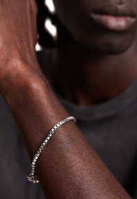 Silver chain bracelet with rectangular links, polished finish, worn on a dark-skinned wrist against a neutral background.